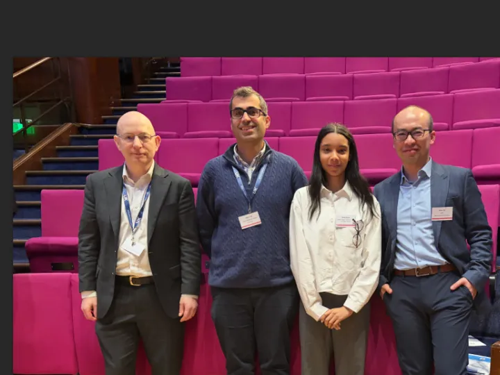 Four people stand in front of chairs in a lecture theatre. 