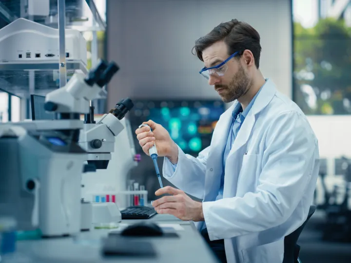 man with pipette in lab, alognside microscope