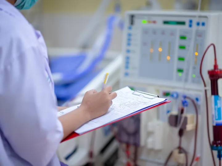 Dialysis nurse checking machine, writing on clipboard 