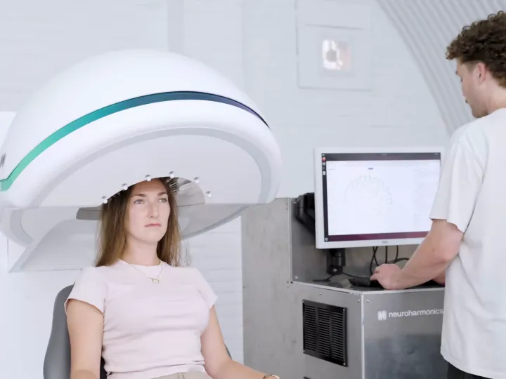 Woman sits under machine that wraps around her head while clinician stands next to her looking at computer