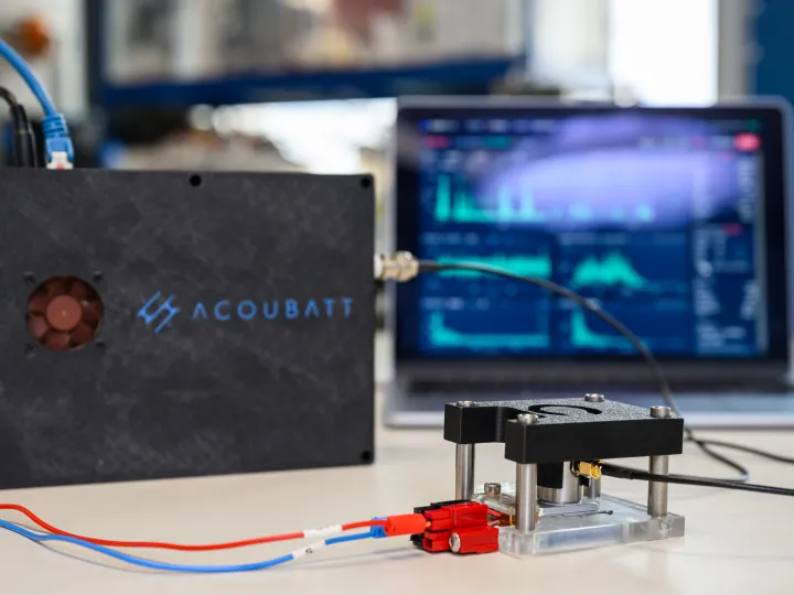AcouBatt product - bbox connected with wired to batteries with computer screen showing graphs and data in the background