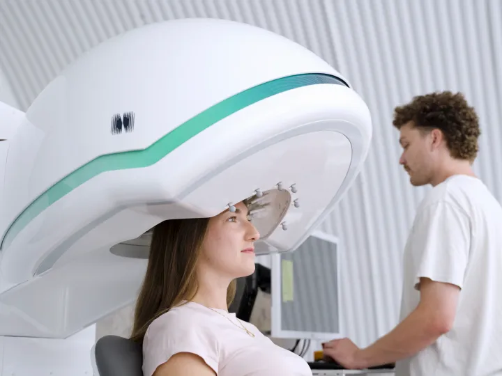 Woman sits beneath ultrasound head machine while clinician stands by at a computer