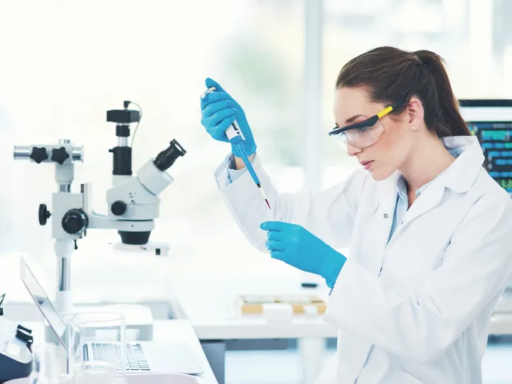 Young female scientist wearing protective glasses while pouring a test sample into a vile inside of a laboratory