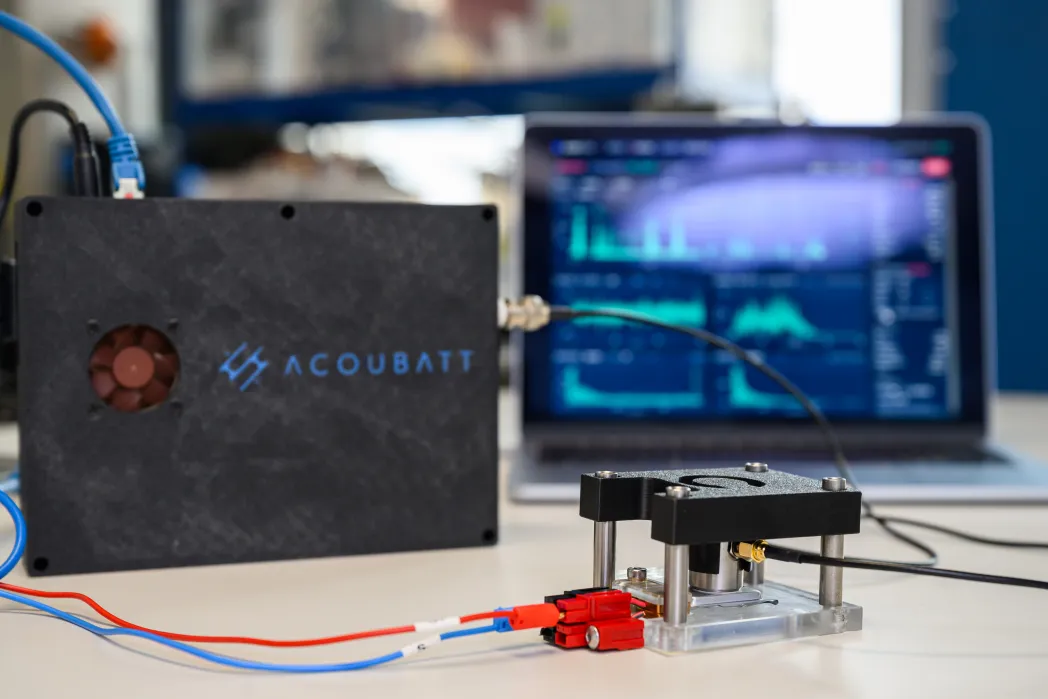 AcouBatt product - bbox connected with wired to batteries with computer screen showing graphs and data in the background