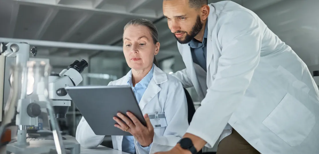 man and older woman look at ipad in lab coats