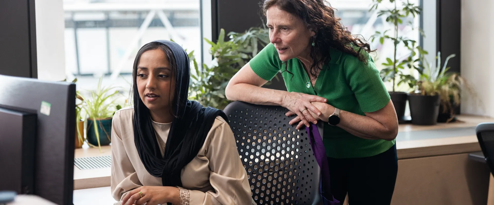 two women, one seated and one standing leaning over, looking at a computer at UCL 