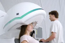 Woman sits beneath ultrasound head machine while clinician stands by at a computer