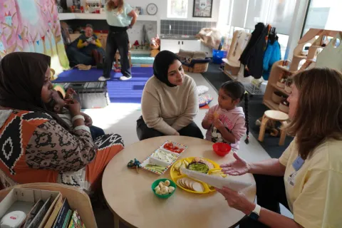 two mothers and their toddler children at a table eating food