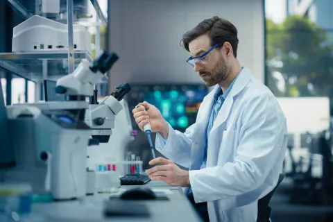 man with pipette in lab, alognside microscope