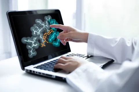 Closeup of researcher hand pointing at a laptop screen displaying 3D molecular model