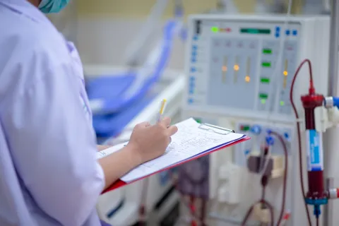 Dialysis nurse checking machine, writing on clipboard 