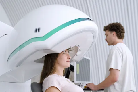 Woman sits beneath ultrasound head machine while clinician stands by at a computer