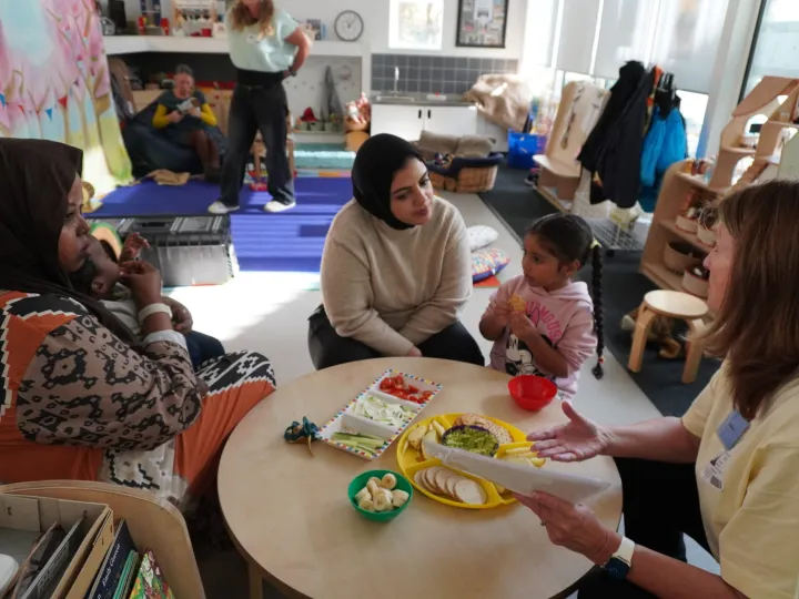two mothers and their toddler children at a table eating food