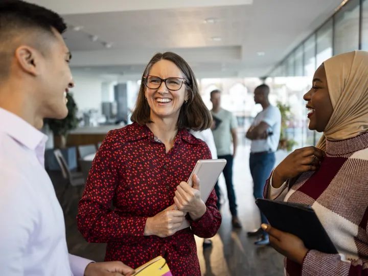 Lady holding a notepad smiles at two other people.