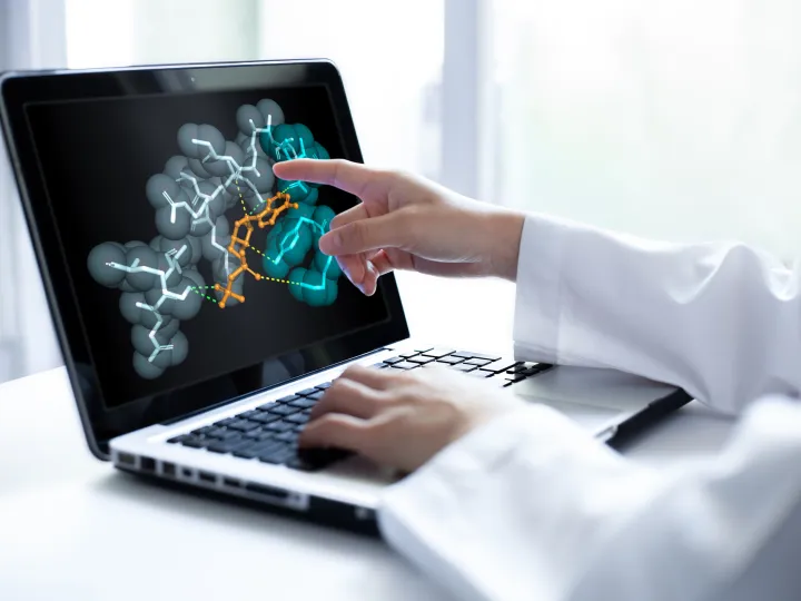 Closeup of researcher hand pointing at a laptop screen displaying 3D molecular model